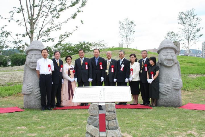 2体の石像の間に並んで序幕後の記念撮影をしている10人の男女の写真