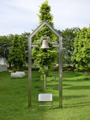 樹木の前の芝生の上に立っている鐘のモニュメントの写真