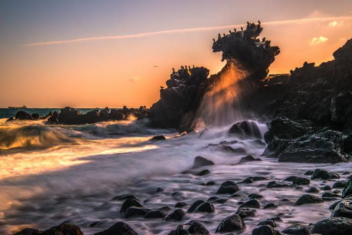 夕日で赤く染まった海辺の龍頭岩の写真