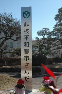 銀色の柱で三田市のロゴマークと「非核経和都市さんだ」と銘打った等標柱の写真