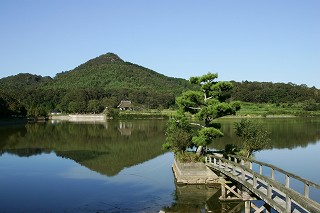 新緑の有馬富士と福島大池の風景写真。風の凪いだ水面には「逆さ富士」の映る様子が確認できる