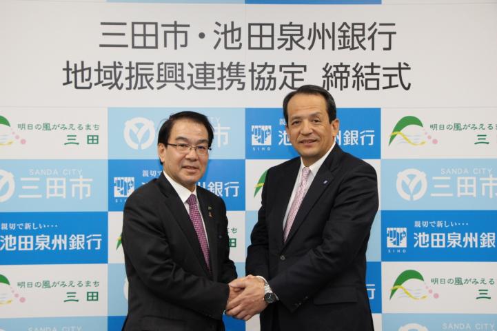 協定式にて池田泉州銀行の藤田頭取と握手を交わす森市長の写真