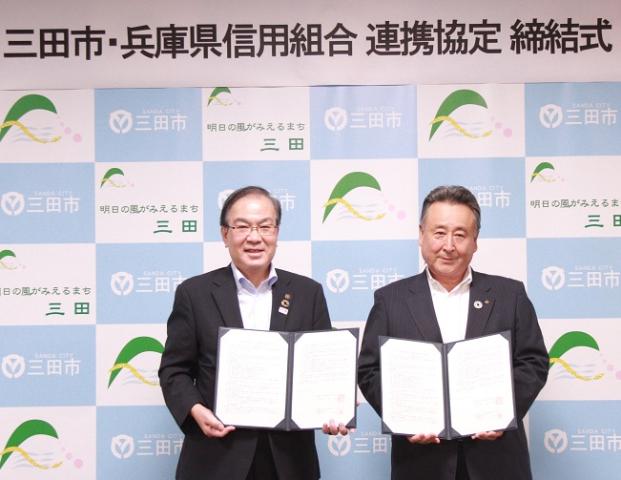 締結式にて署名した調印書を手に記念撮影に応じる、森市長と河田経営本部長の写真