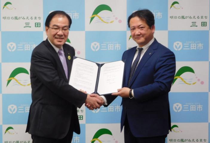 協定締結式にて調印書を手にしつつ握手を交わす、森市長と藤原支店長の写真