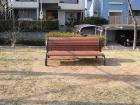 枯れた芝生の上に置かれた木製の椅子のような背伸ばしベンチの写真