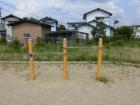 砂地のような場所に3本のポールが立っていてその間を高さの違う鉄棒が付けられているアームトレーナーの写真