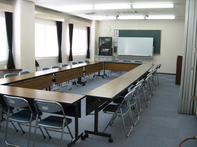 明るい蛍光灯で照らされた4つの長机が四角形に配置されてある会議室の写真