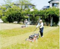 帽子を被った作業員が公園の草刈りをしている写真