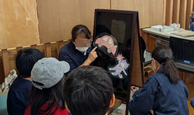 大人2人が紙芝居をしており、子供たちが見物している