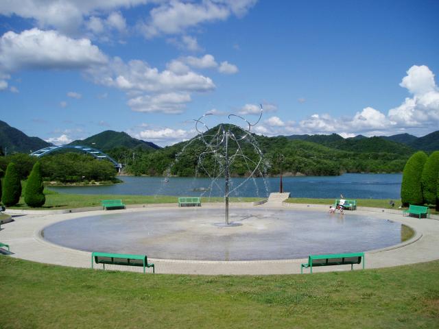 晴天の山が連なる中心にある公園に円形にベンチが置いてある写真