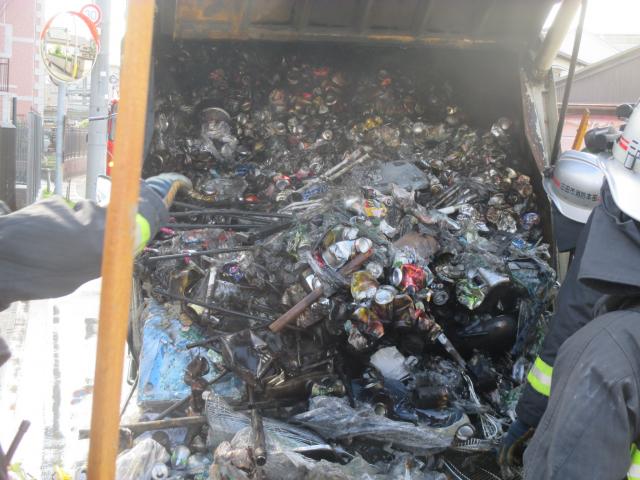 ゴミ収集車から黒い発火した後の缶などを取り出す消防員たちの写真