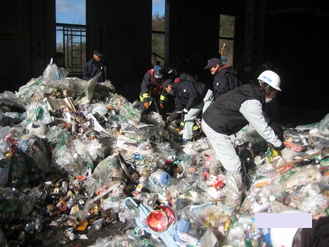 ゴミ袋に入ったゴミの山の中を作業員たちが消防署の検証をしている写真