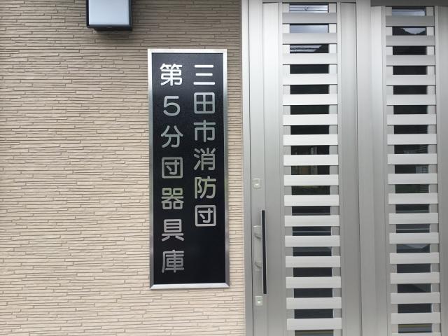 建物の扉の横に、「三田市消防団第5分団器具庫」と書かれた看板がかかっている写真