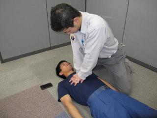 スマホを床に置き、寝ている男性に心臓マッサージをしている男性の写真