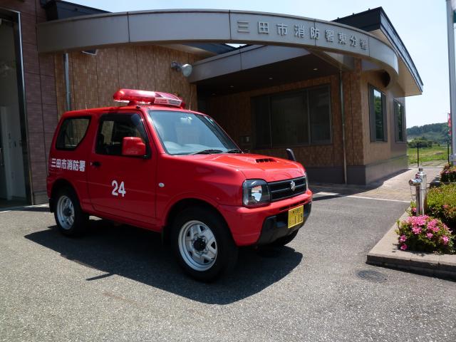 施設の入り口の前に、赤い軽自動車が停まっている写真