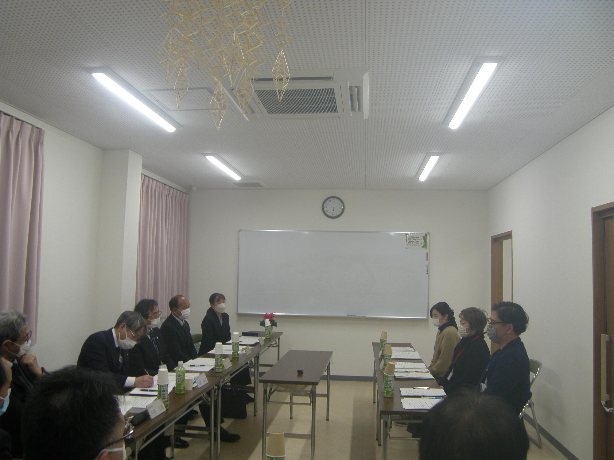 中央に花の飾られた机がありその周りを囲うように並べられた机と席で行われている教育懇談会の写真