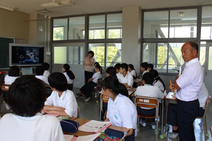 ビデオを見ながらグループ学習ををしている様子の中学生と、見学している教育委員の写真