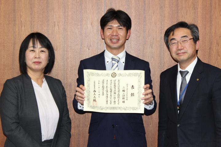三輪三四郎主幹教諭が兵庫県優秀教職員表彰の表彰状を笑顔でカメラに向けている写真