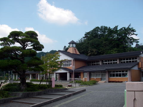 木々に囲まれており黒い屋根と白と褐色の壁をもつ、三田市立母子小学校校舎の外観の写真