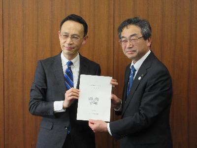 スーツを着た男性がスーツを着た男性に書類を渡している写真