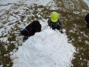 雪を集めて山を作って遊ぶ園児達の写真
