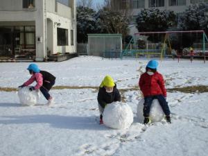雪で大きな玉を作って遊ぶ園児達の写真