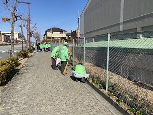 緑の制服を着たスタッフが道路脇に花を植えている写真