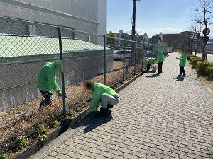 緑の制服を着たスタッフが花を植える為に道路脇を整備している写真
