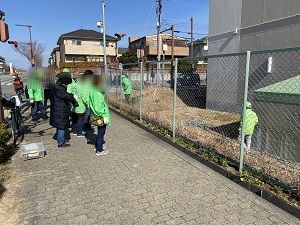道路脇の花を植え終わり片づけをしている緑色の制服を着たスタッフ達の写真