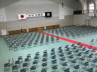 整然と並べられた数多くのパイプ椅子の中央に赤いレッドカーペットが敷かれた体育館を、斜め上から映した写真