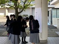 校舎の柱に貼られた紙を見ている、制服姿の女子生徒たちの写真