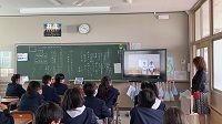 教室内で黒板横のモニターに映る先輩のプレゼンテーションを真剣に見る生徒たちの写真