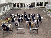 中庭で楽譜を広げ制服姿で楽器を演奏する生徒たちの写真
