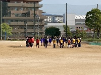 広いグラウンドの一角で円形になって立っているジャージ姿の生徒たちの写真