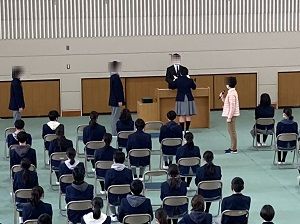 パイプ椅子に座る生徒たちの前で生徒が卒業証書を受け取っている様子の卒業式の写真