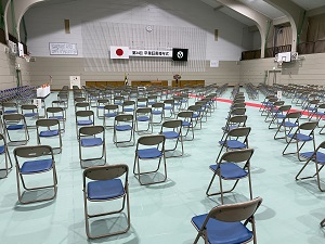 体育館に薄水色のシートが敷かれ、パイプ椅子がいくつも等間隔に並べられている卒業式会場の写真