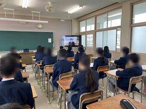 教室に生徒たちが机に座り、右側に設置されたモニターを見ている様子の写真