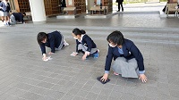 校舎の入り口で膝をつき雑巾で床を拭いている、制服姿の3人の女子生徒の写真