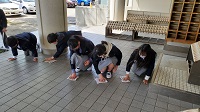 校舎の入り口でしゃがみながら雑巾で床を拭いている、制服姿の生徒たちの写真