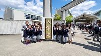 校門前の入学式と書かれた立て看板の横で、ピースサインをしている生徒たちの写真