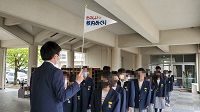 旗を持って前に立つ先生に向かい制服姿の生徒たちが2列になり整列している写真