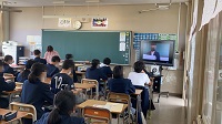 教室内に生徒たちが座り、右側に設置されたモニターに映し出された生徒を見ている様子の写真