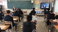 教室内に生徒たちが座って、右側のモニターを眺めている様子の写真