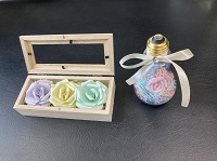 淡い紫、黄色、緑色のバラが小さなガラス付きの木箱に詰められている作品と、ガラスの電球に花が詰められている作品の写真