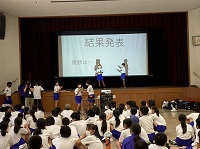 「結果発表」とプロジェクターに表示されステージ上に2人の生徒が立っている様子の写真