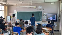 生徒たちが教室に座り、2人の男子生徒が立っている様子の写真
