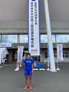 陸上競技大会の垂れ幕の前に立つ、青いユニフォームを着た選手の写真