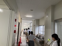 複数の生徒が机と椅子を運んでいる廊下の写真