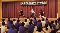 白と黒のジャージ姿の3人の生徒たちが両手を大きく広げて踊っている様子の写真