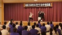 舞台上で白と黒のジャージ姿の生徒たちが頭を抱えるような動きで踊っている様子の写真